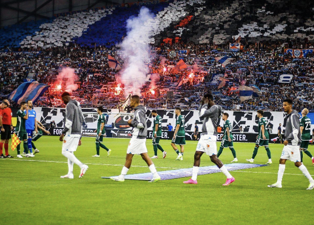 Joueurs de l’OM qui rentre sur le terrain à domicile avec les supporters qui allument des fumigènes en tribunes