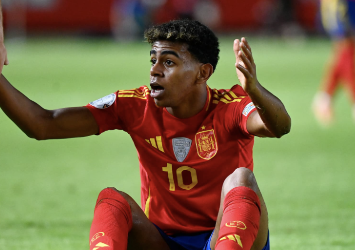 Lamine Yamal assis sur le terrain lève les mains et interpelle l’arbitre pour réclamer une faute pendant un match avec l’Espagne