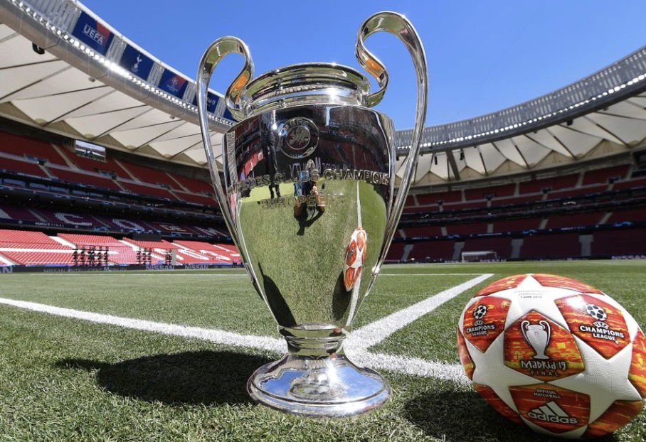 Trophée de la Ligue des Champions posé sur le terrain avec un ballon de football