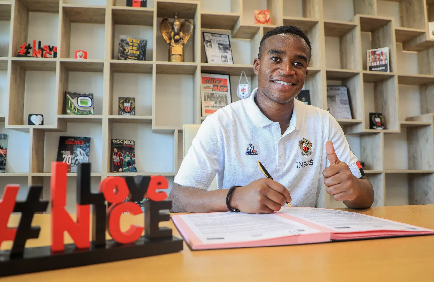 Youssoufa Moukoko stylo en main fait un signe avec son pouce lors de sa signature à l’OGC Nice